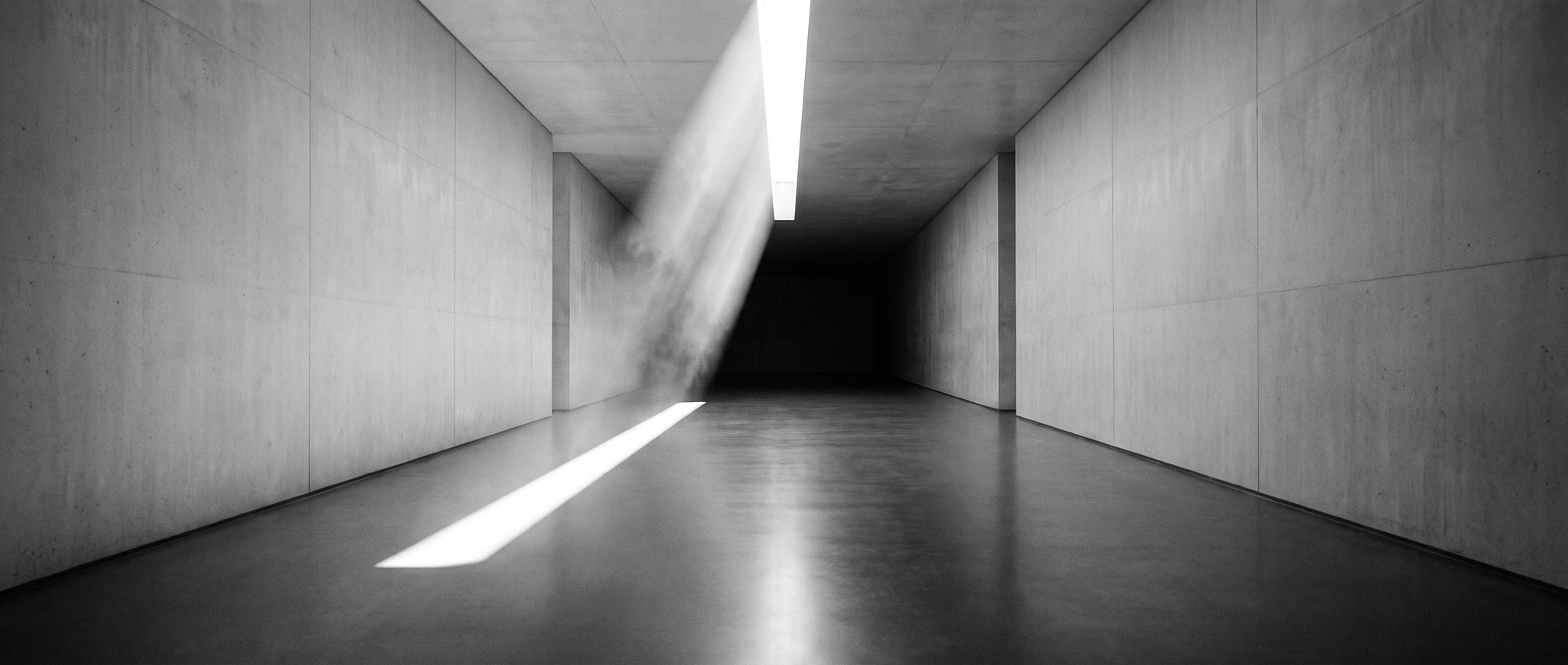 Monochromer futuristischer Lichtkorridor: eine weiße Lichtbahn fällt durch einen Deckenschlitz in eine leere Galerie